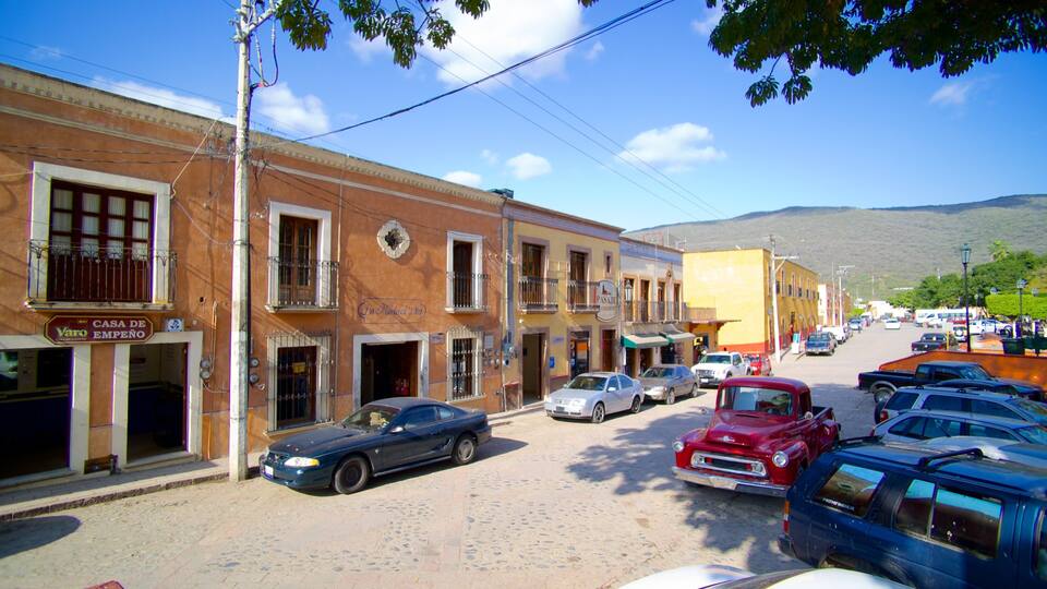 A street lined with historic buildings, parked cars, and a mountainous backdrop.