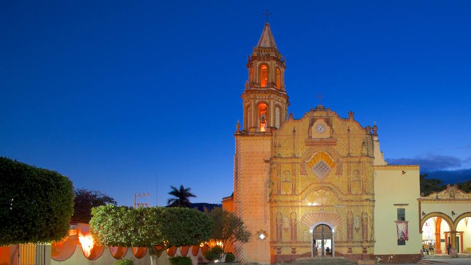 A historic church with a bell tower and ornate facade, surrounded by trees and a well-lit street.