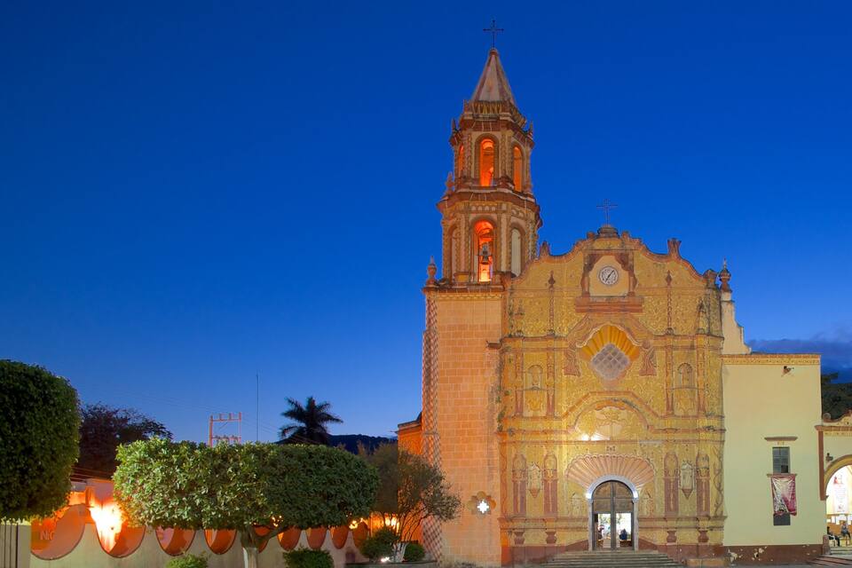 A historic church with a bell tower and ornate facade, surrounded by trees and a well-lit street.