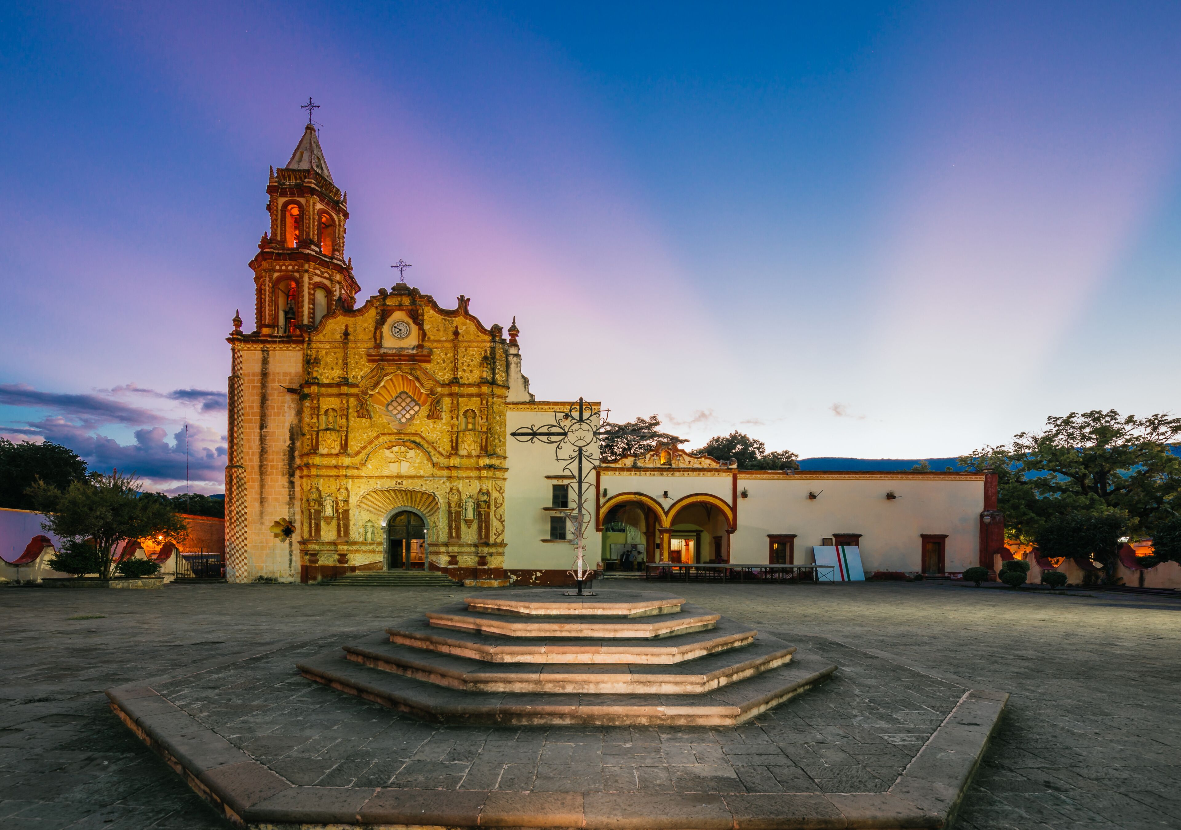 A historic church with a bell tower, a courtyard with steps, and a clear sky.