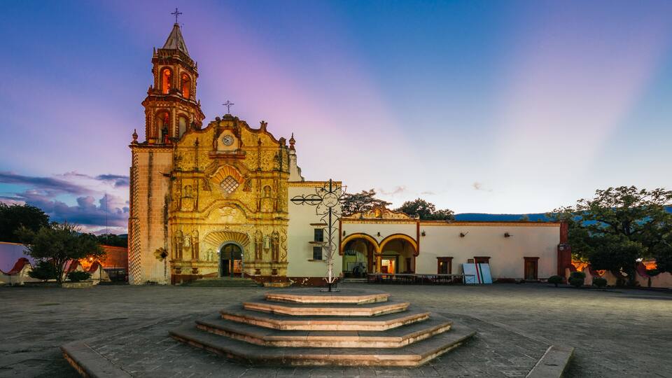 A historic church with a bell tower, a courtyard with steps, and a clear sky.