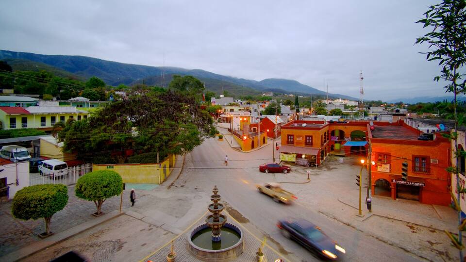 A town square with a fountain, buildings, and a mountainous backdrop.