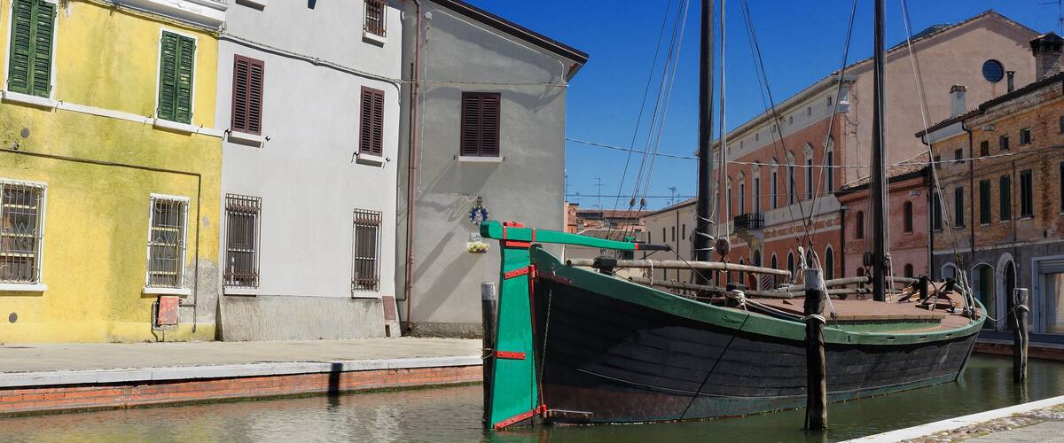 Un canal con un bote verde amarrado en un muelle, rodeado de edificios históricos con fachadas rojas y blancas.