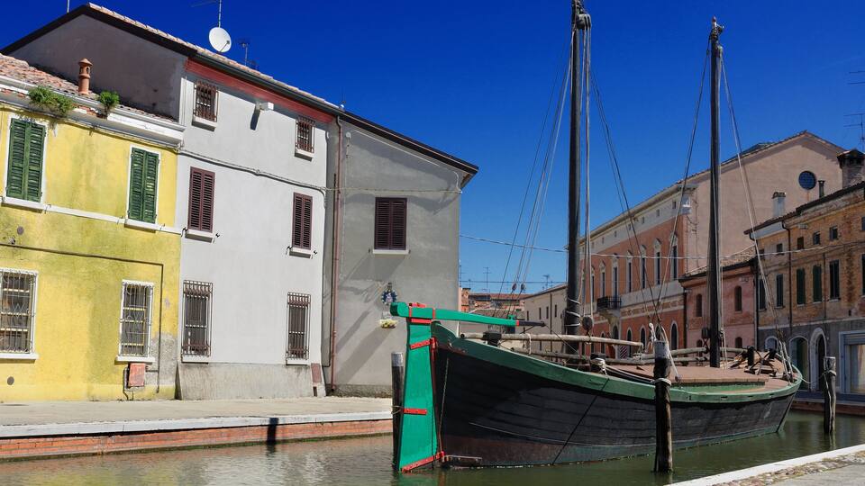 A canal with a green boat docked at a pier, surrounded by historic buildings with red and white facades.