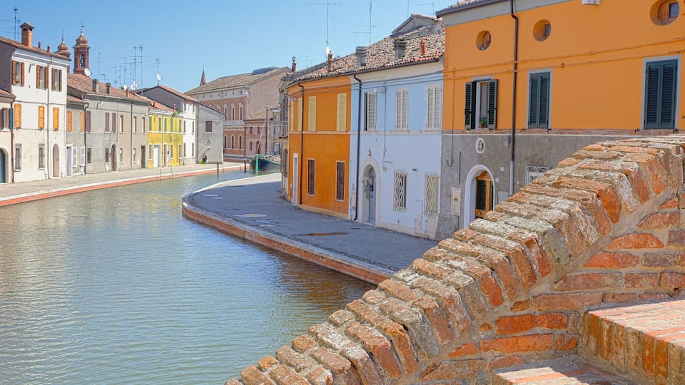 A canal with buildings on either side, a stone bridge, and a clear blue sky.