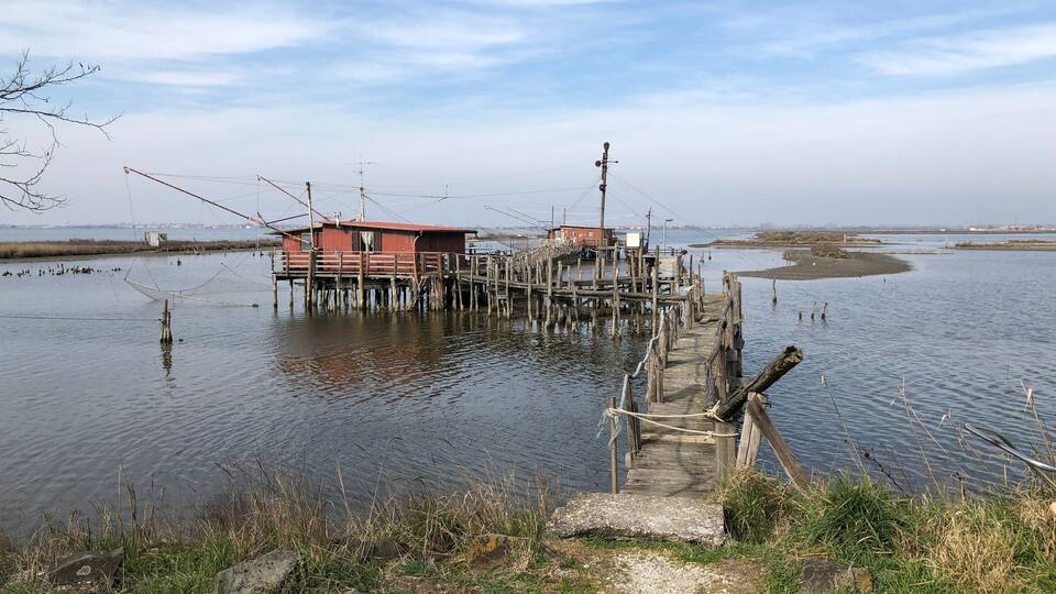 A wooden pier leading to a red building on stilts over calm water.
