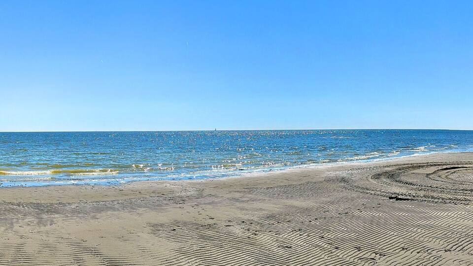A beach with gentle waves, a clear sky, and a distant lighthouse.