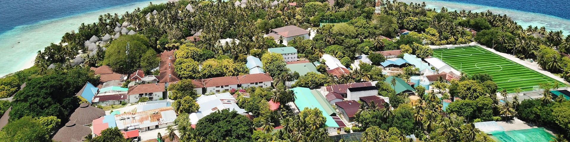 A tropical island with a clear blue sea, surrounded by lush greenery and small buildings.