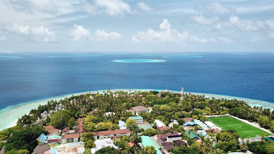 A tropical island with a clear blue sea, surrounded by lush greenery and small buildings.