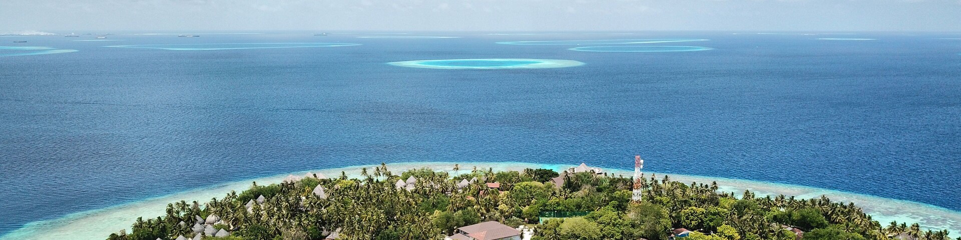Una isla tropical con un mar azul cristalino, rodeada de exuberante vegetación y pequeñas construcciones.