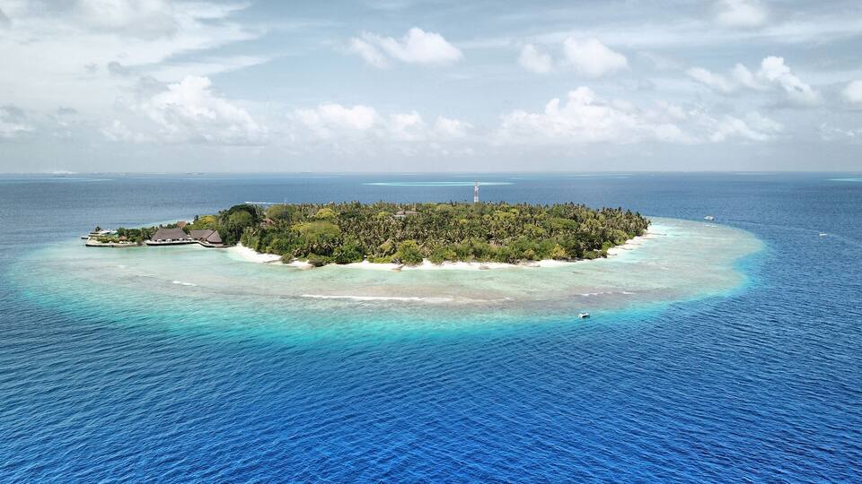 A tropical island surrounded by turquoise waters, featuring a lighthouse and overwater bungalows.