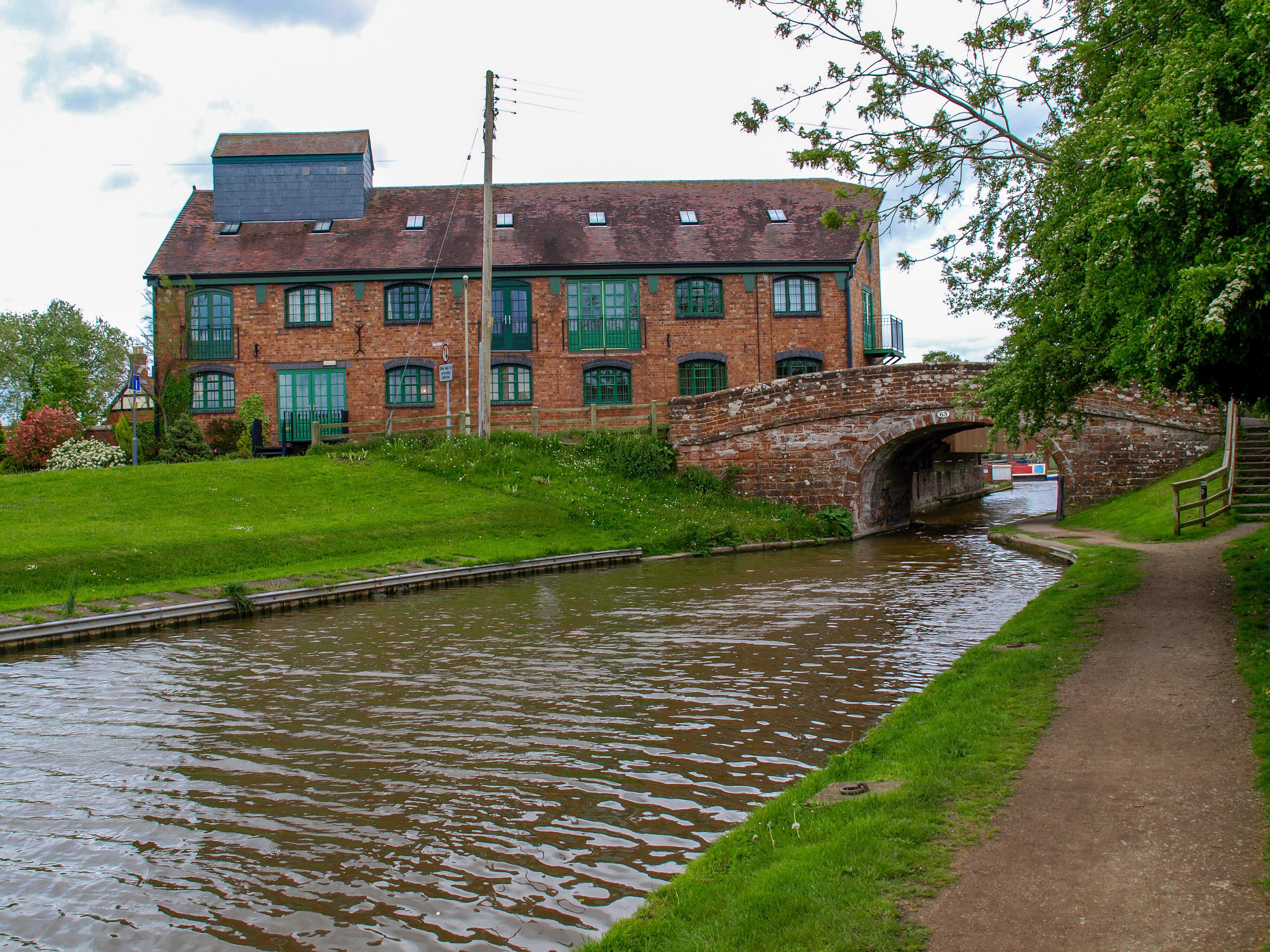 A brick building with green shutters, a narrow canal, and a small bridge.