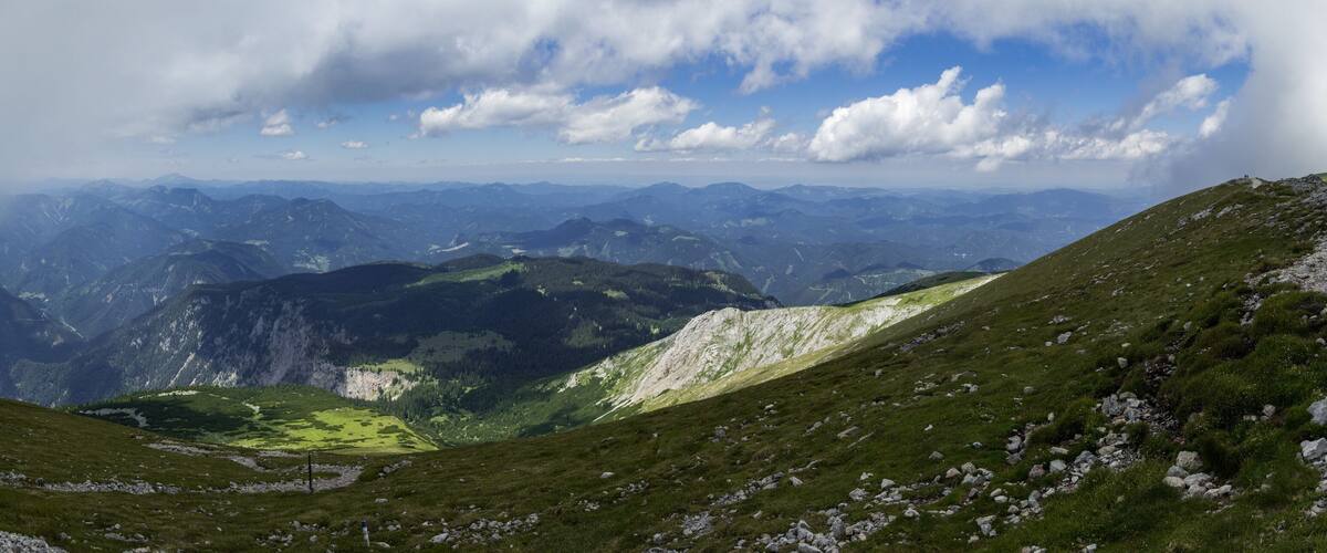 A mountainous landscape with green valleys and rocky peaks under a partly cloudy sky.