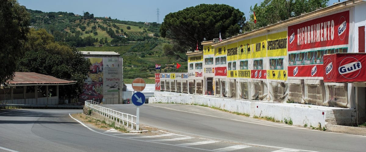 A road with a 'no entry' sign, a billboard with 'Gulf' advertisements, and a building with 'Targa Florio' branding.