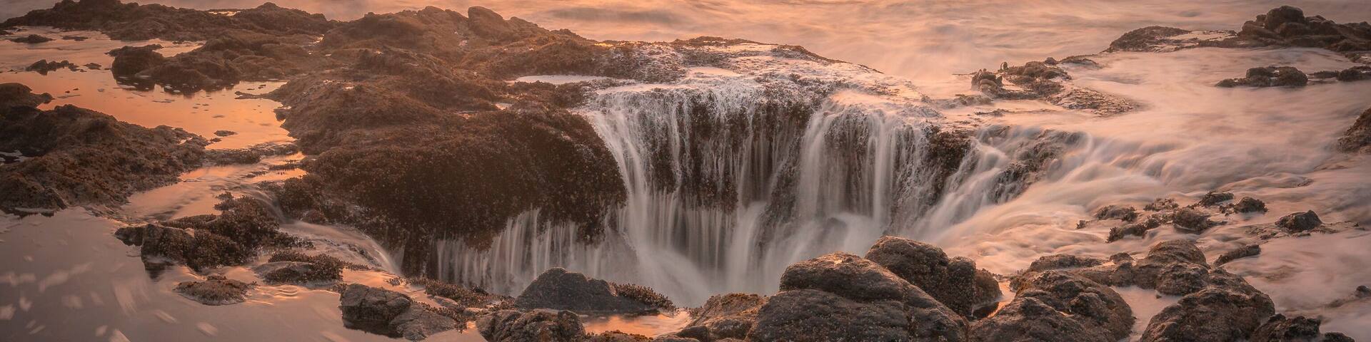 View of thor's well at sunset with dramatic waves and rugged rocks, Yachats, Oregon, United States.