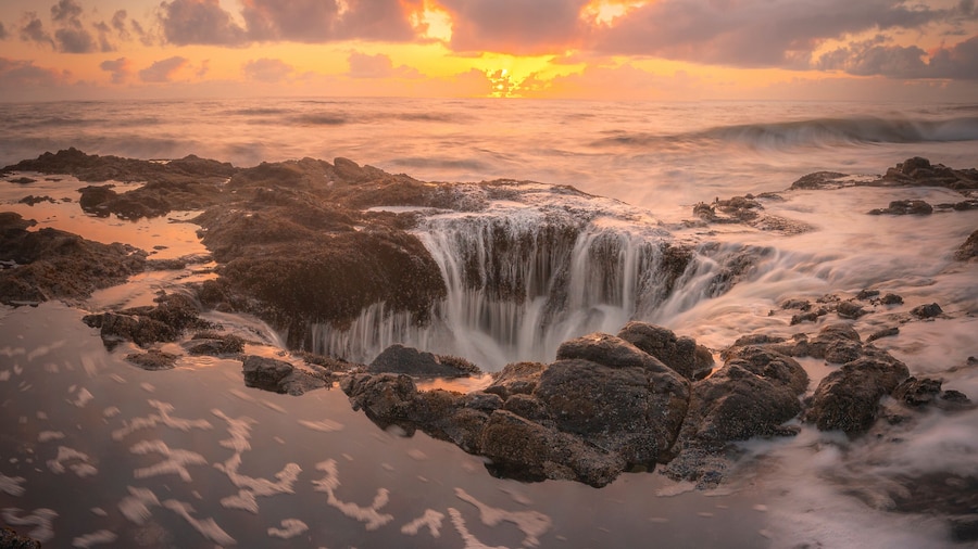 View of thor's well at sunset with dramatic waves and rugged rocks, Yachats, Oregon, United States.