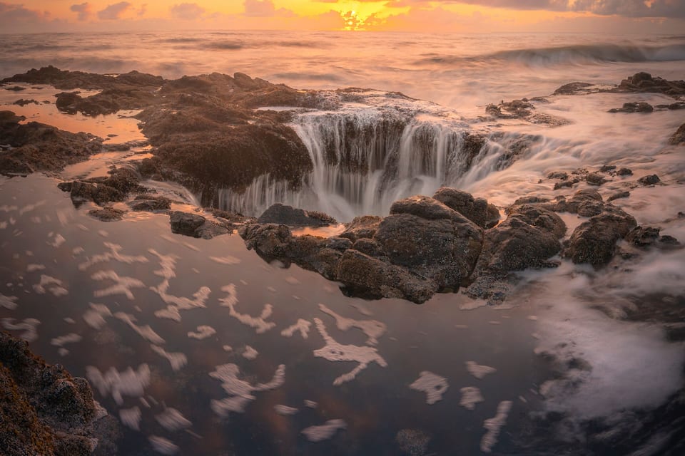 Una cascada rodeada de terreno rocoso y un atardecer.