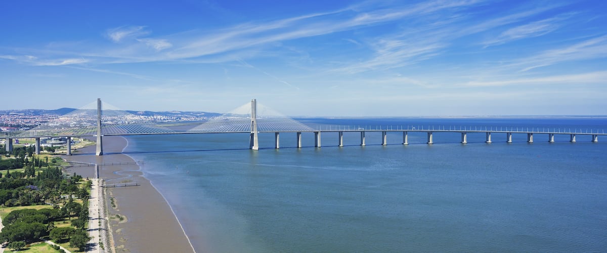 A large suspension bridge spanning a wide river, with a cityscape in the background.