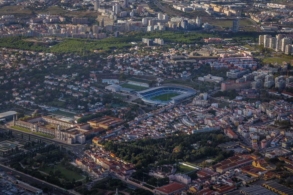 An aerial view of a city with a large stadium, dense residential areas, and surrounding greenery.
