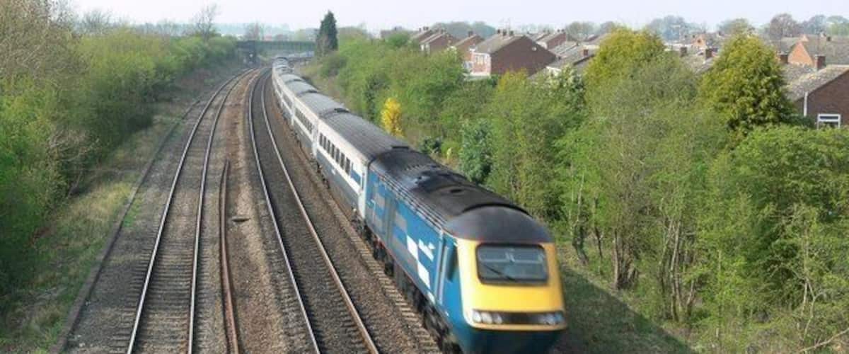 A train on railway tracks surrounded by greenery and houses.