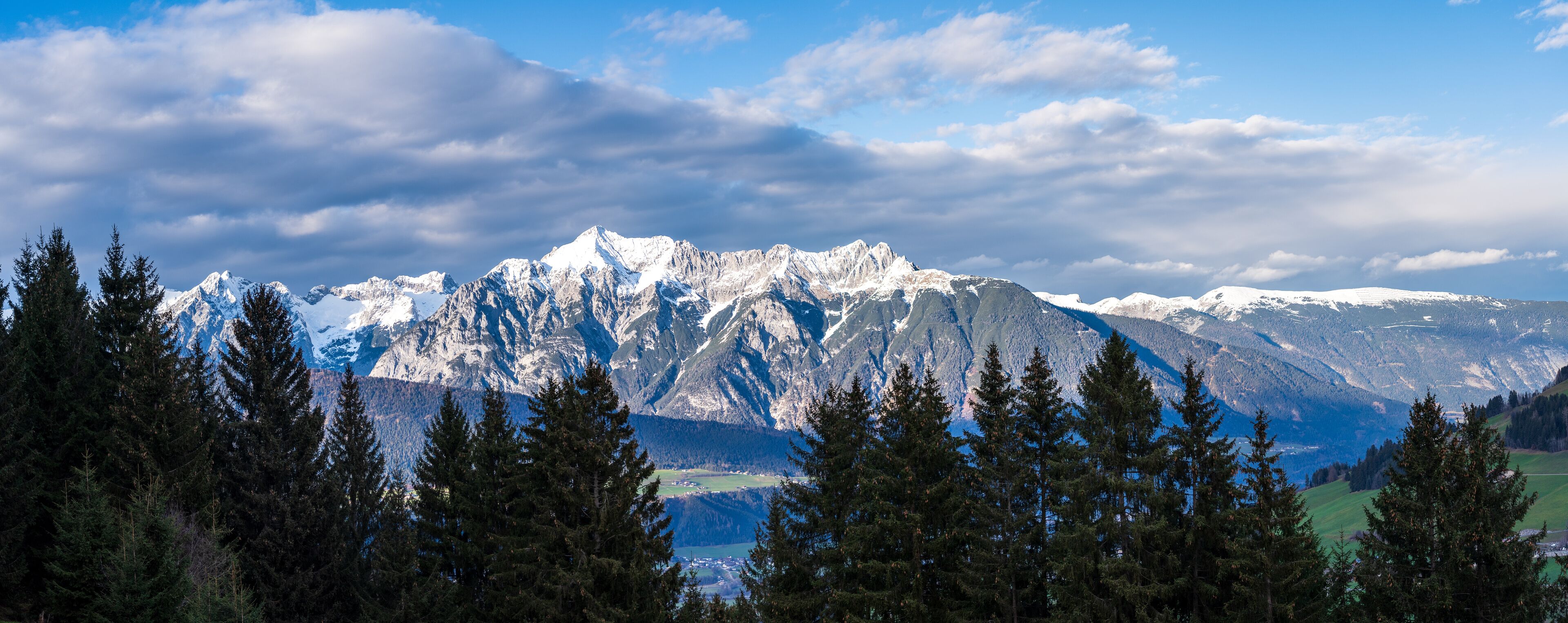Cordillera montañosa con picos nevados, denso bosque de coníferas y un cielo azul despejado.