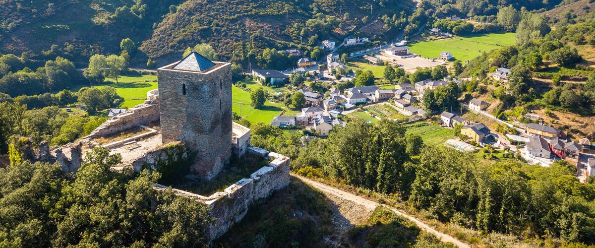 A medieval tower amidst a village surrounded by lush green hills.