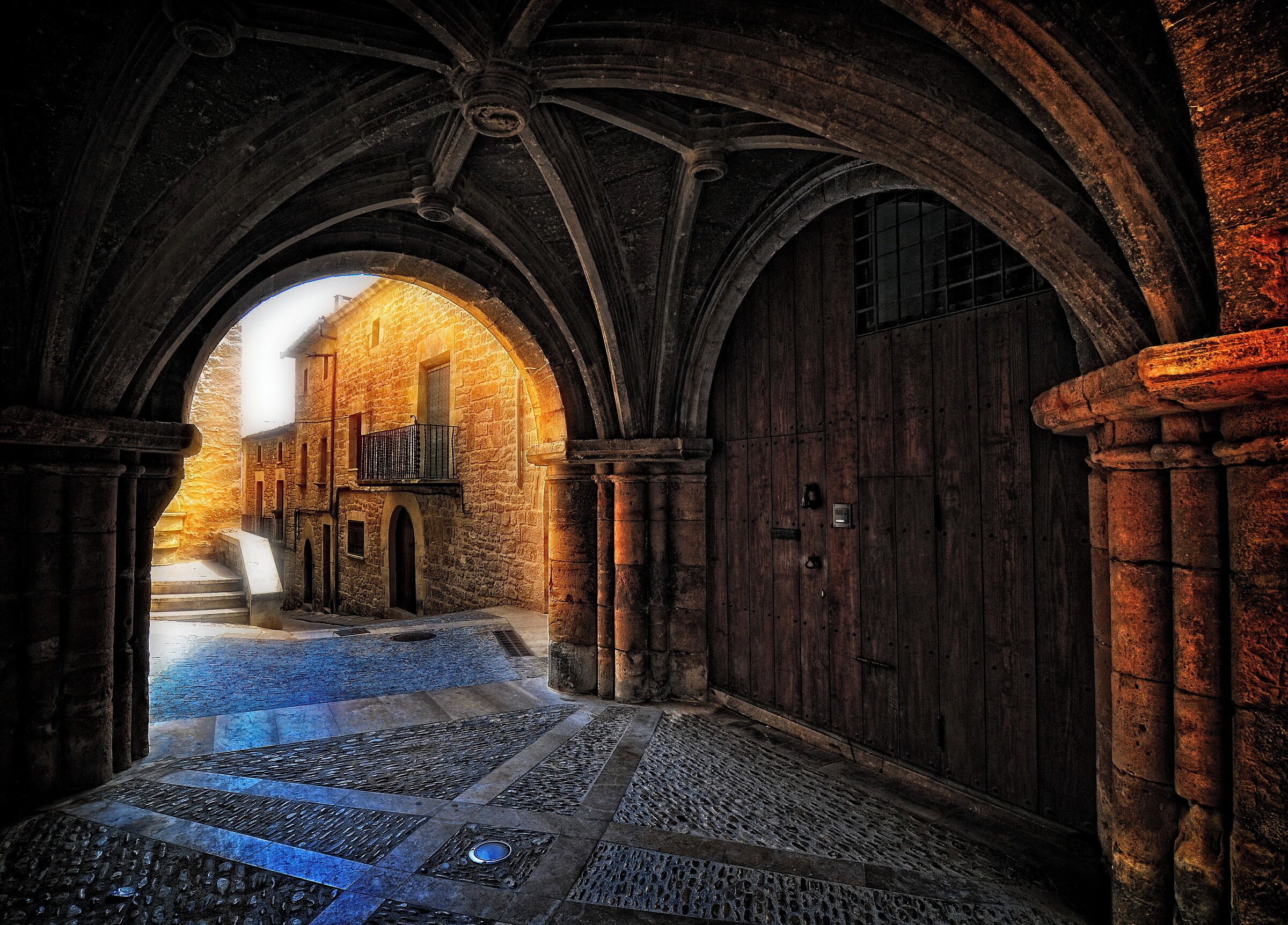 An arched stone corridor with a wooden door and a small balcony.