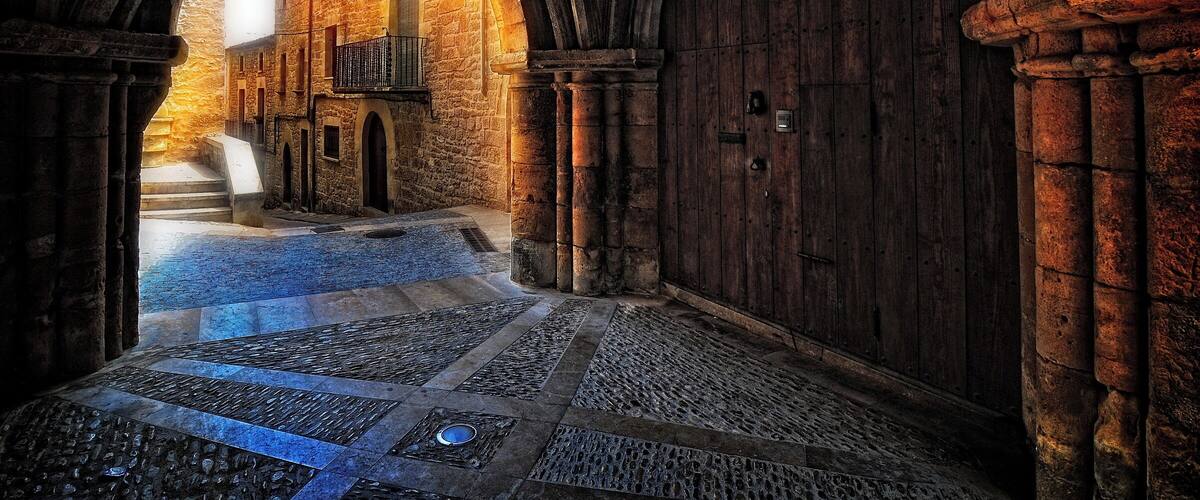An arched stone corridor with a wooden door and a small balcony.