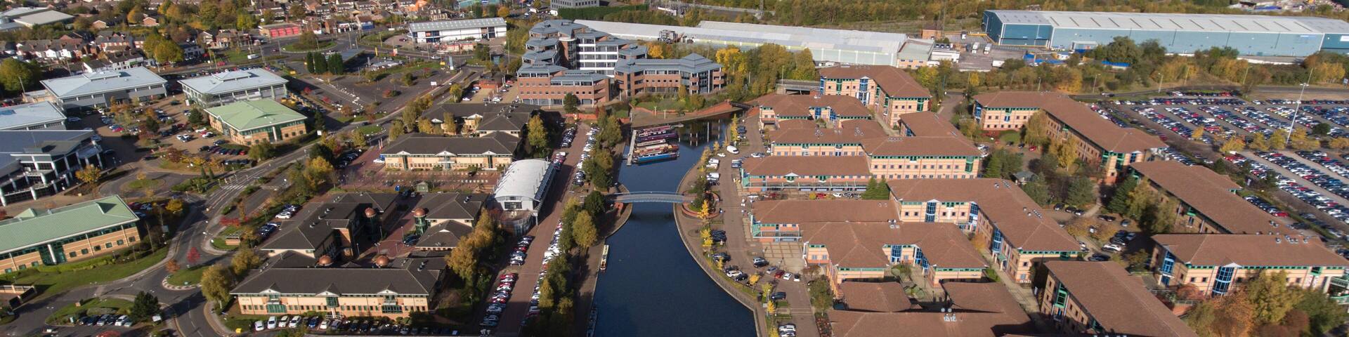 An aerial view of a city with a river, buildings, and a parking lot.