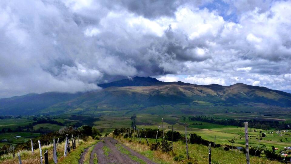 A dirt road leading to a mountain range under a cloudy sky.