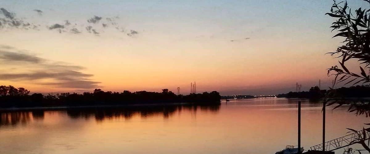 A calm river at sunset with a dock and trees on the right.
