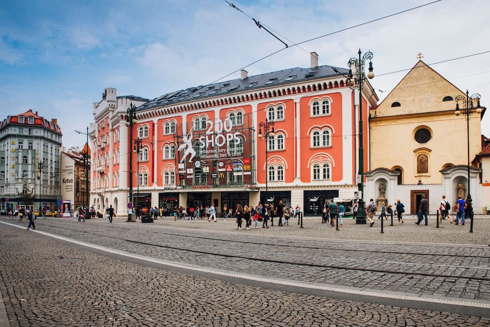 A cobblestone street with a red building labeled "200 Shops" and a yellow church.