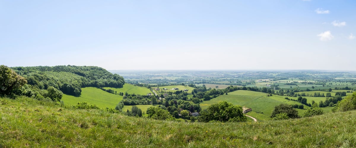 A tower on a hill overlooking a valley with fields and a distant town.
