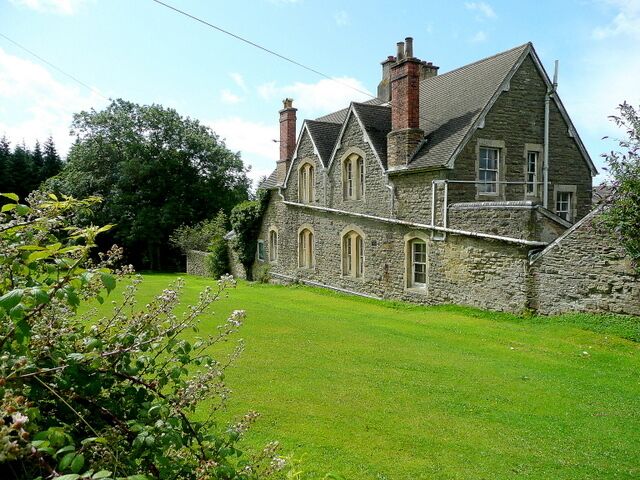 A stone building with a sloped roof and chimneys, surrounded by a well-maintained lawn and trees.