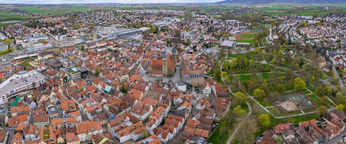 An aerial view of a densely built town with historic buildings, a church, and a large open field.