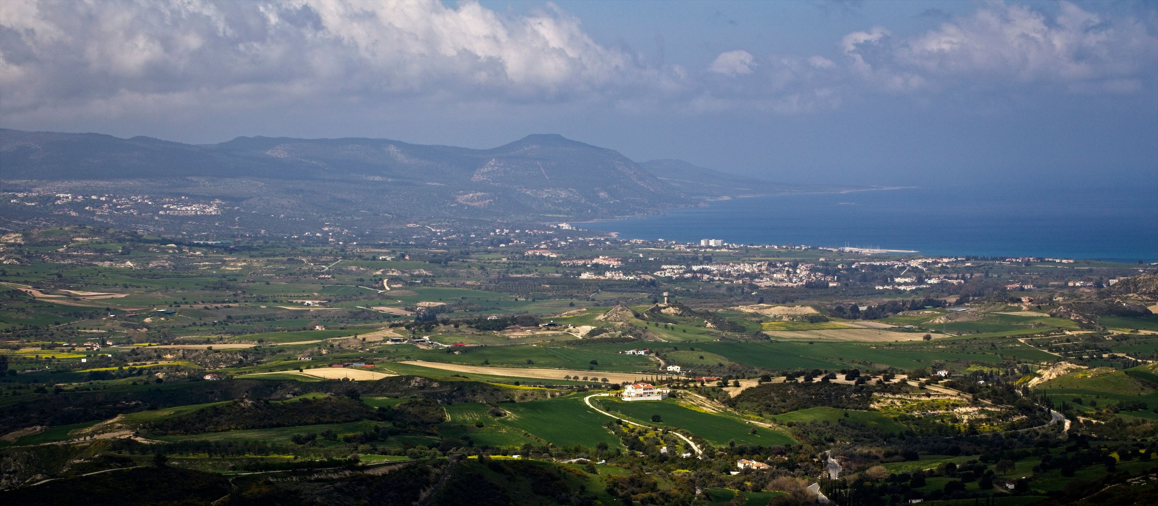 A coastal landscape with rolling hills, a winding road, and a distant view of the sea.