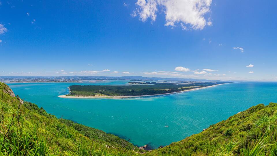 A coastal landscape with a clear blue sky, turquoise waters, and green hills.