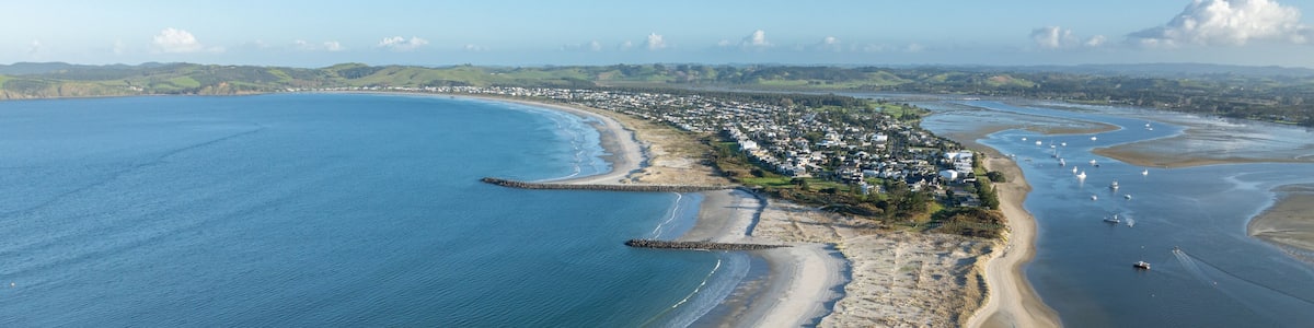 An aerial view of a coastal town with a curved bay, sandy beaches, and a rocky breakwater.