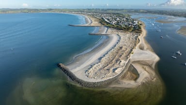 An aerial view of a coastal town with a curved bay, sandy beaches, and a rocky breakwater.