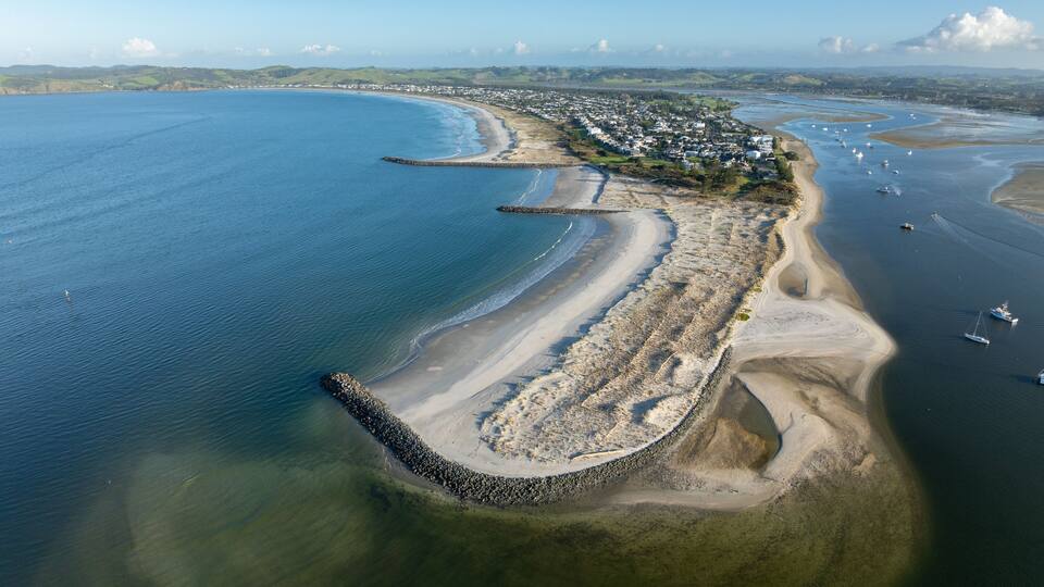 An aerial view of a coastal town with a curved bay, sandy beaches, and a rocky breakwater.