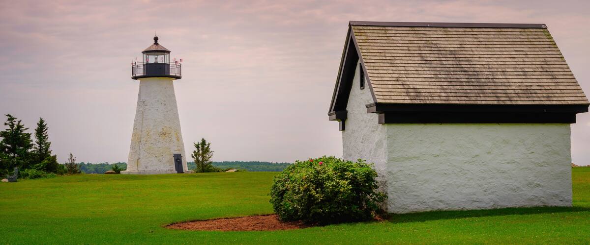 A lighthouse and a white building with a brown roof in a grassy area.