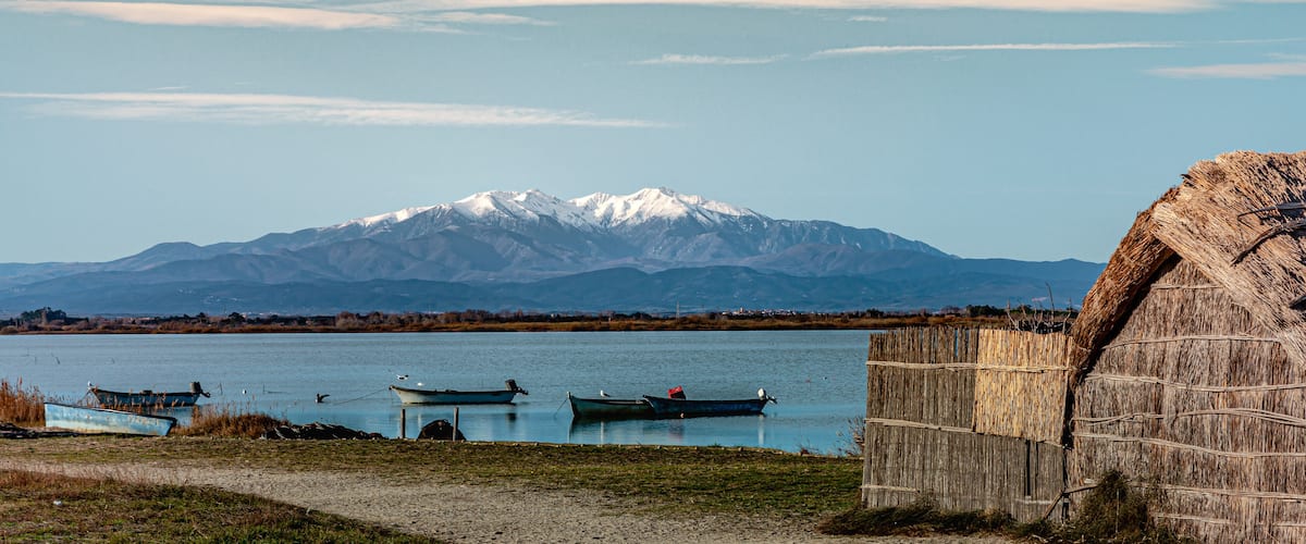 A lake with boats, a wooden structure, and a snow-capped mountain in the background.
