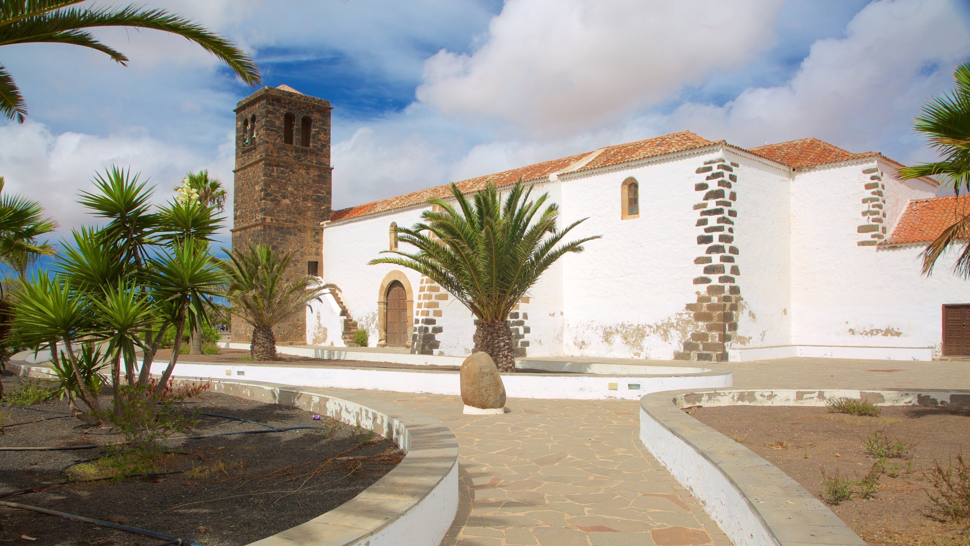 A white church with a stone bell tower, palm trees, and a stone pathway.
