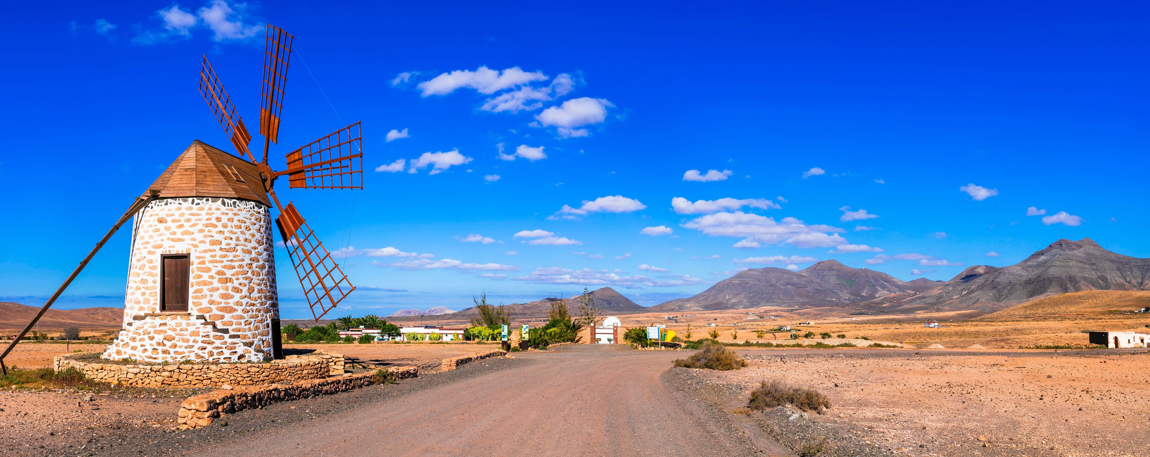 A stone windmill, a dirt road, and mountains in the background.
