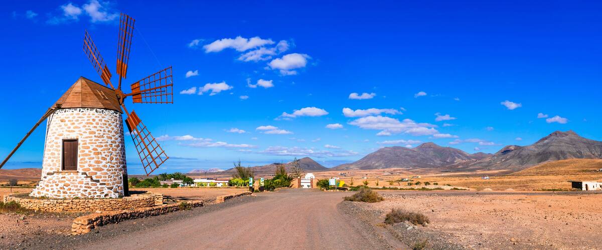 Un molino de piedra, un camino de tierra y montañas al fondo.