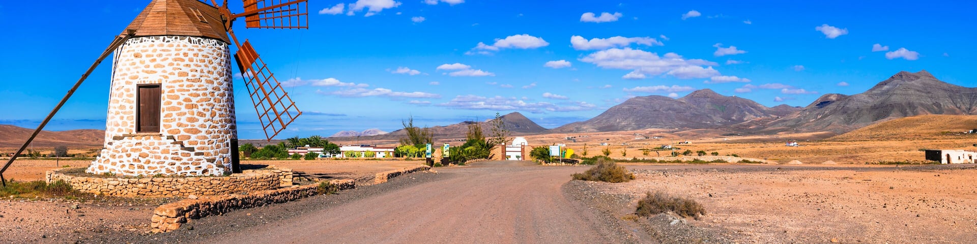 A stone windmill, a dirt road, and mountains in the background.