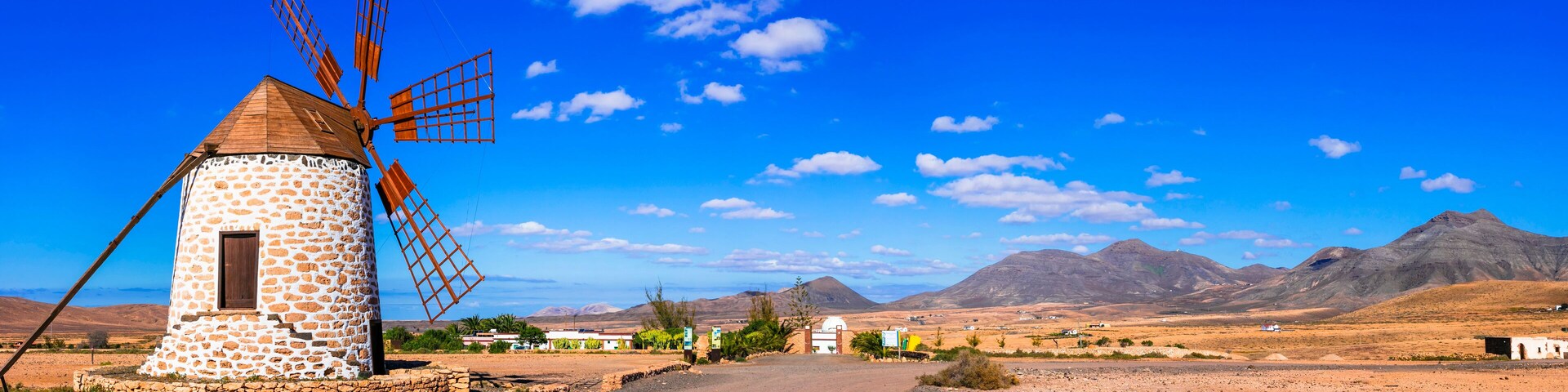 Un molino de piedra, un camino de tierra y montañas al fondo.