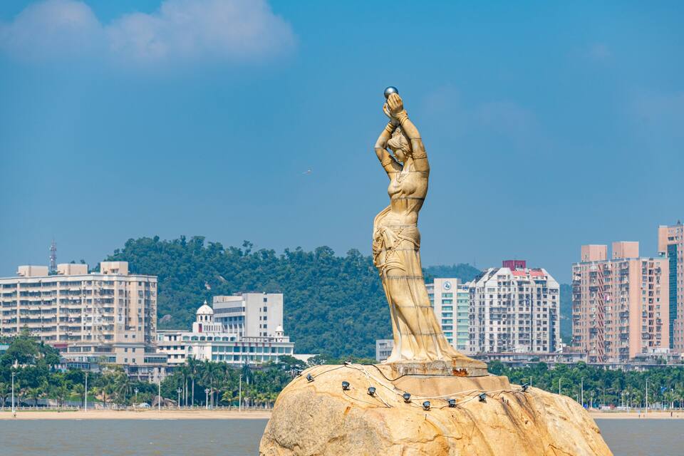 A statue on a rock with a cityscape in the background.