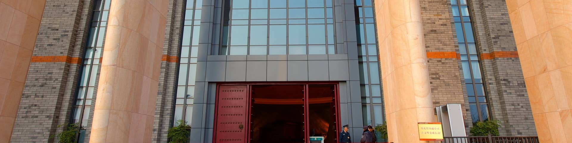 A building facade with large columns, a prominent red flag with a hammer and sickle symbol, and a red door.