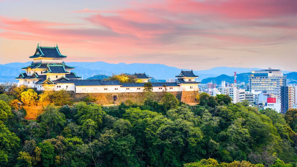 A traditional Japanese castle with multiple tiers, surrounded by lush greenery and mountains in the background.